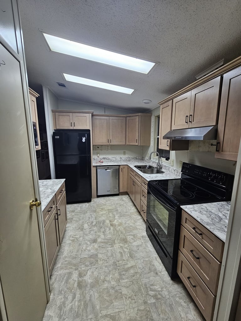 Kitchen remodel with light shaker-style cabinetry, gray-veined countertops, black range and stainless steel dishwasher.