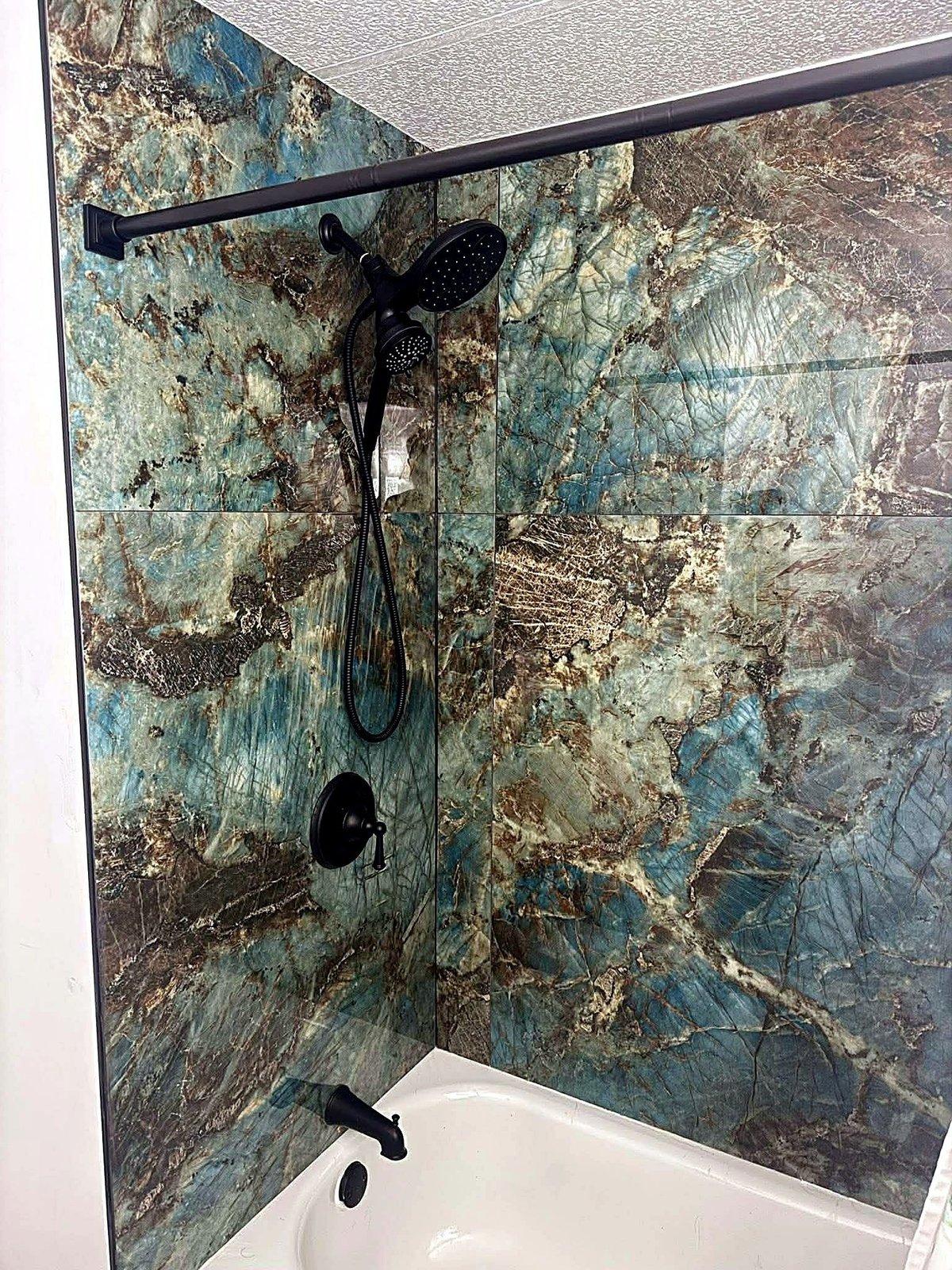 Lakewood Ranch bathtub with large-format blue-green patterned wall tile and black shower fixtures