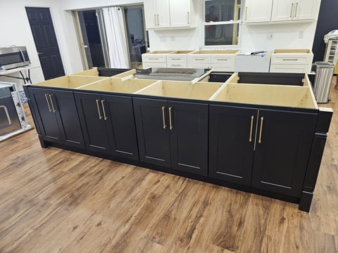 Large dark kitchen island with shaker-style cabinet doors, drawer storage and brass-toned hardware.