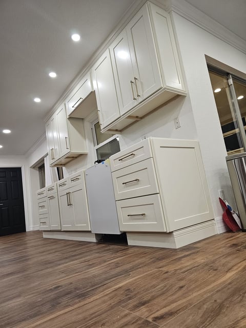White shaker cabinetry with brass-toned pulls and warm wood-look flooring in a kitchen renovation.