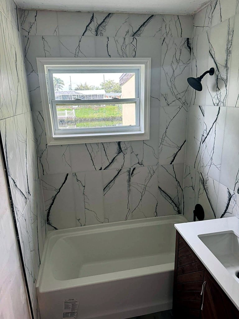 Venice tub surround with white marble-look tile, dark veining and black fixtures during finishing work.